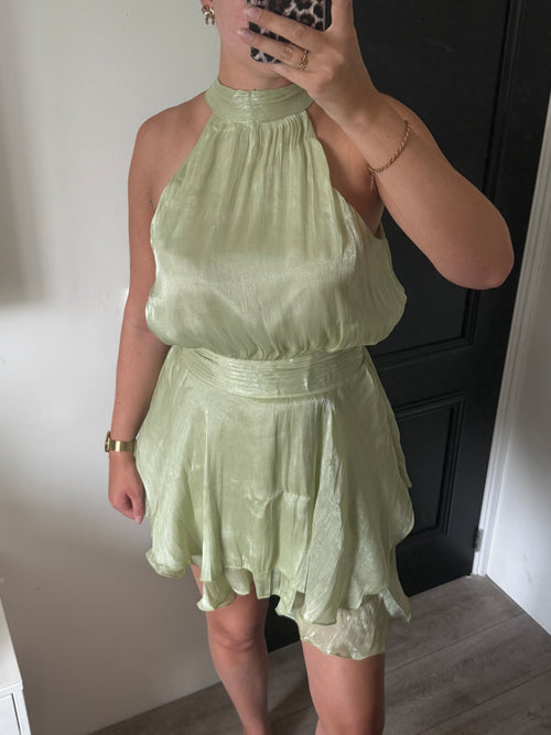 Faye Dress in saliegroen, een elegante halterjurk met glanzende stof en asymmetrische rok.