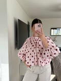 Een lichtroze polka dot blouse met grote bordeauxrode stippen, hoge hals en open rug met striksluiting.
