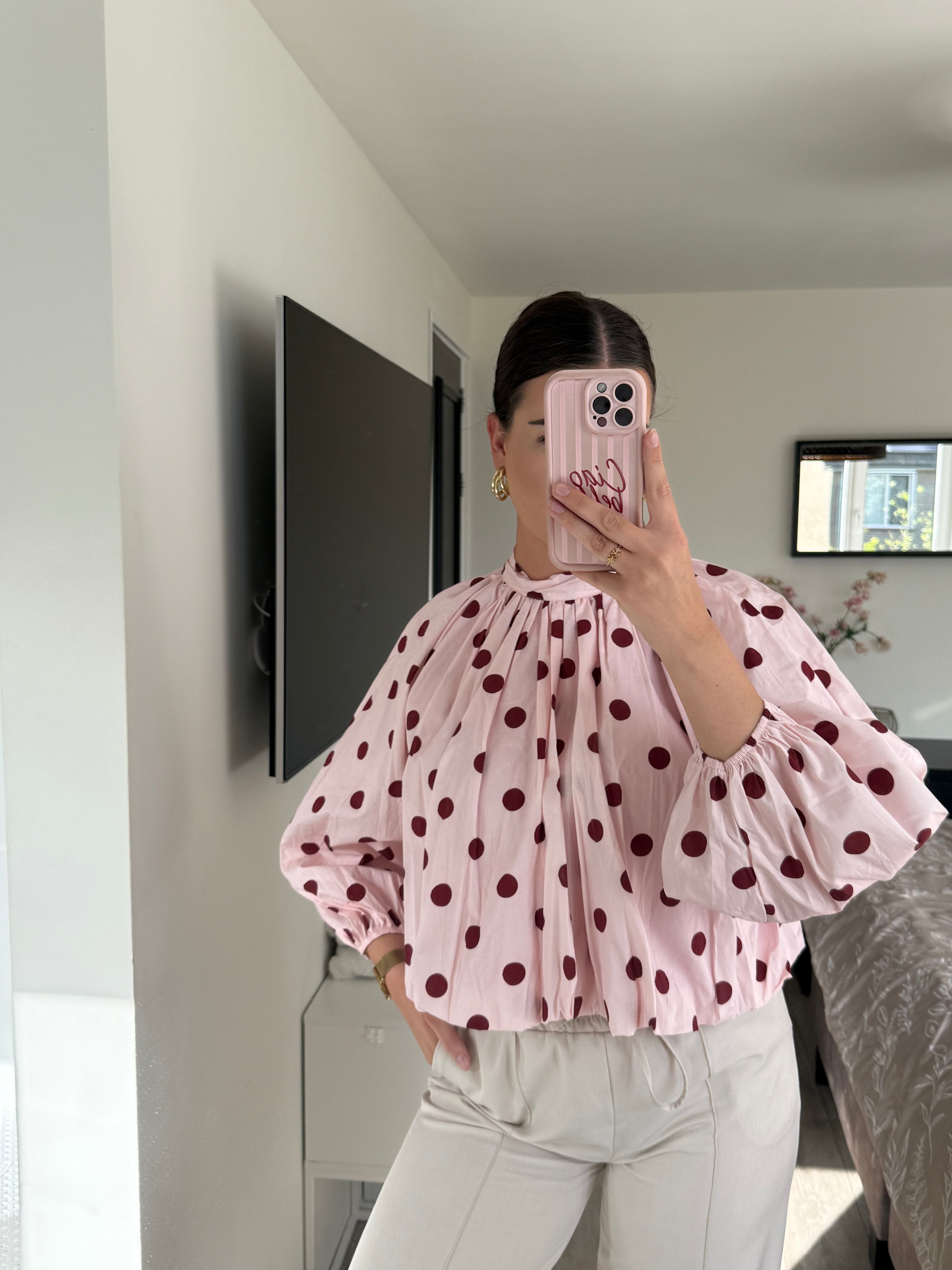 Een lichtroze polka dot blouse met grote bordeauxrode stippen, hoge hals en open rug met striksluiting.