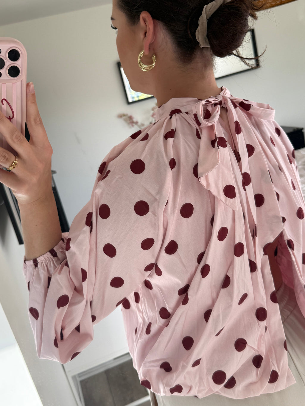 Detail van de achterzijde van de roze polka dot blouse met een open rugpand, een elegante striksluiting in de nek en bordeauxrode stippen.